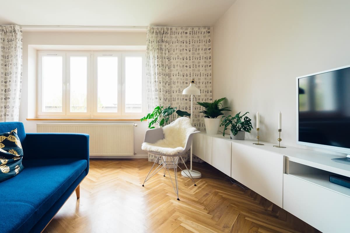 Living con sillón azul, ventana con cortinas estampadas y piso de parquet en espiga